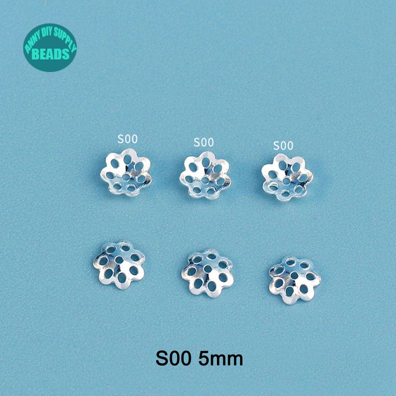 May include: Six silver-colored, flower-shaped bead caps with multiple holes, arranged on a light blue surface. The text "S00 5mm" is at the bottom. The top left corner has a logo that says "Anny DIY Supply Beads".