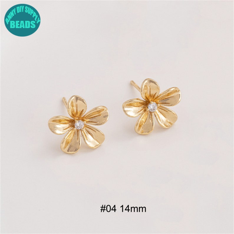 K&ouml;nnte beinhalten: Ein Paar goldene Ohrringe in Blumenform mit einem kleinen, klaren Strassstein in der Mitte jeder Blume. Die Ohrringe sind 14 mm gro&szlig; und mit #04 gekennzeichnet.