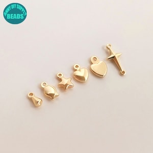 May include: A set of six gold-toned metal charms, including a heart, star, cross, teardrop, and two different flower shapes. The charms have a shiny finish and are designed for jewellery making.