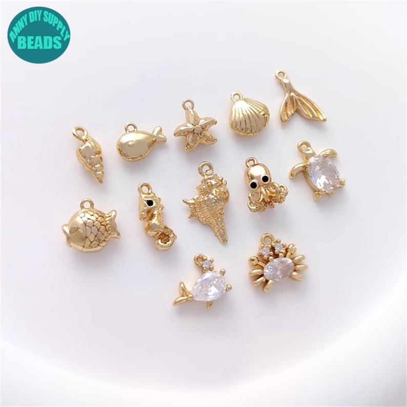 Puede incluir: Una colecci&oacute;n de 12 abalorios de metal dorado con varios dise&ntilde;os de vida marina, incluyendo una estrella de mar, una concha, un pulpo, un pez, un caballito de mar y un cangrejo. Algunos abalorios tienen diamantes de imitaci&oacute;n transparentes.