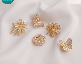 May include: Five gold-toned metal embellishments with clear crystal accents. The embellishments include a flower, a butterfly, and three different styles of round flowers.