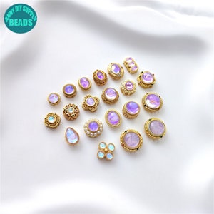 Puede incluir: Surtido de cabujones de vidrio iridiscente morado y dorado con engastes de metal dorado ornamentados. Los cabujones son de varias formas, incluyendo redonda, ovalada, de lágrima y de flor.