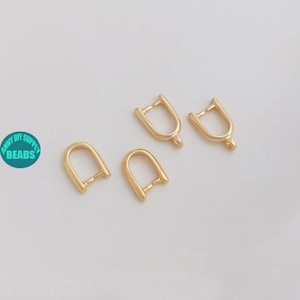 Può includere: Quattro elementi di gioielleria dorati a forma di U con un piccolo anello in basso. Gli elementi sono disposti su una superficie bianca. Il testo "ANNY DIY SUPPLY BEADS" è in un cerchio in basso a sinistra.