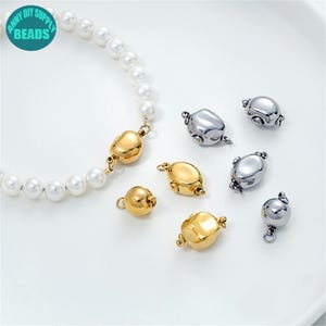 May include: A white pearl necklace with a gold clasp is displayed alongside several gold and silver magnetic clasps. The clasps are various shapes and sizes, perfect for jewelry making. The image includes a teal circle with the text "ANNY DIY SUPPLY BEADS".