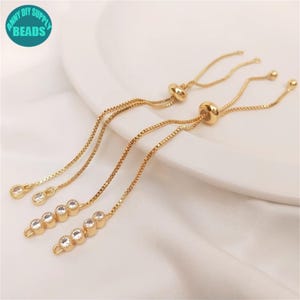 Könnte beinhalten: Drei goldene Kettenarmbänder mit verstellbaren Schiebeknoten und klaren Kristall-Akzenten.