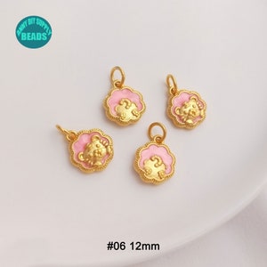 May include: Four gold-colored bear charms with pink enamel accents. Each charm is 12mm in diameter and features a bear design within a scalloped frame. The charms have a small loop for attaching to jewelry.
