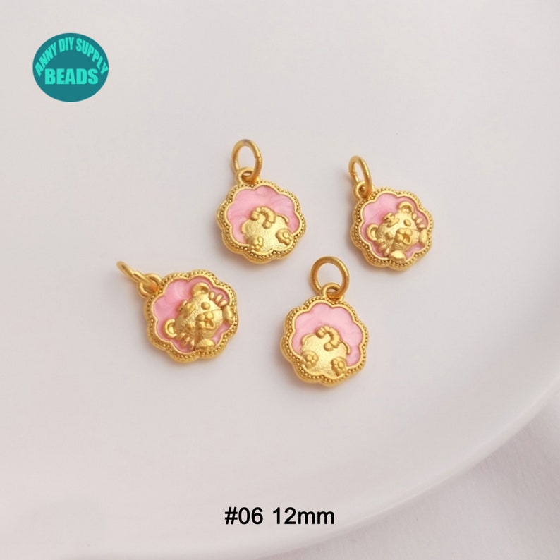 May include: Four gold-colored bear charms with pink enamel accents. Each charm is 12mm in diameter and features a bear design within a scalloped frame. The charms have a small loop for attaching to jewelry.