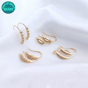 May include: Four pairs of gold-toned earring hooks featuring a curved design encrusted with small clear crystals. Each hook includes a small loop at the bottom for attaching charms or pendants, showcasing a metallic finish and sparkling accents.
