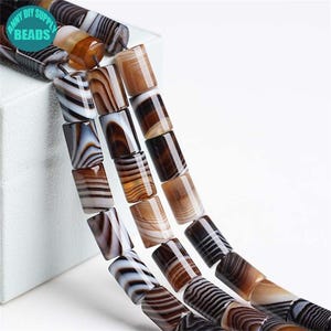 May include: Close-up of rectangular beads in brown, tan, and white with a striped pattern. The beads are strung together. The image includes the text "ANNY DIY SUPPLY BEADS".