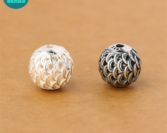 May include: Two silver beads with a decorative, intricate, openwork design. The beads are round and have a hole in the center. One bead is polished and shiny, while the other has a more oxidized finish.