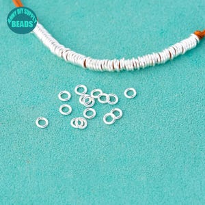 Peut inclure: Gros plan sur un tas de anneaux de saut argentés sur une surface turquoise. Les anneaux de saut sont petits et ronds, et ils sont parfaits pour la fabrication de bijoux.