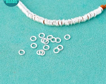 May include: A close-up of a pile of silver jump rings on a turquoise surface. The jump rings are small and round, and they are ideal for jewellery making.