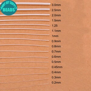 Peut inclure: &Eacute;chantillons de cordons &eacute;lastiques blancs de diff&eacute;rentes &eacute;paisseurs, de 0,2 mm &agrave; 3,0 mm, pr&eacute;sent&eacute;s sur un fond beige. Le texte "ANNY DIY SUPPLY BEADS" est &eacute;galement visible.