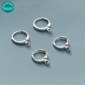 Może przedstawiać: Cztery srebrne kolczyki koła z zapięciem na zawias. Kolczyki mają średnicę około 2,5 cm.
