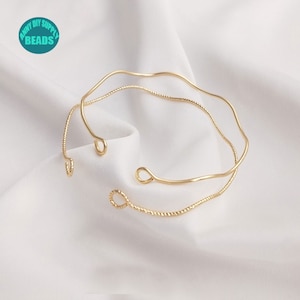Puede incluir: Dos pulseras de metal dorado. Una pulsera tiene un diseño simple y ondulado. La otra pulsera tiene un diseño de cuerda trenzada.