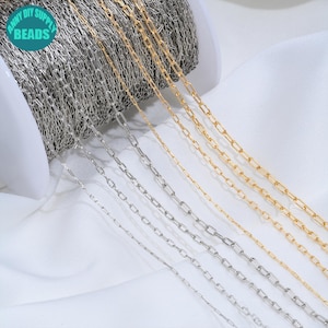 Peut inclure: Une bobine de chaîne en métal argenté et une bobine de chaîne en métal doré, toutes deux composées de maillons ovales allongés. La chaîne argentée est enroulée sur une bobine en plastique blanc et la chaîne dorée est drapée à côté. Logo ANNY DIY SUPPLY BEADS.