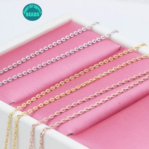 May include: Four different colored chains in a pink box. The chains are silver, gold, rose gold, and a lighter silver color. The chains are all the same length and are arranged in a stack.