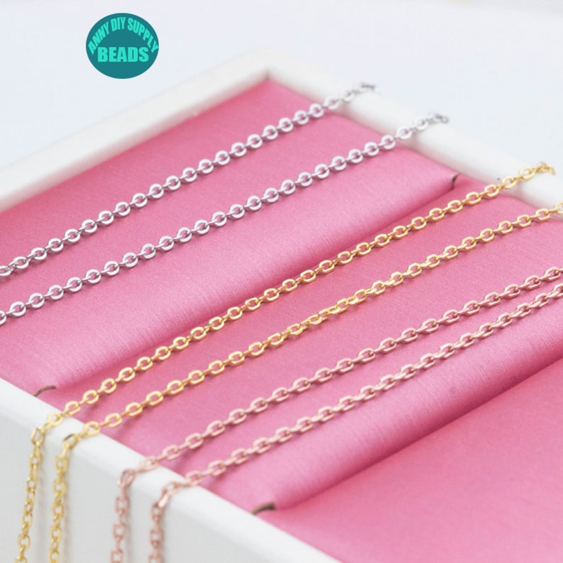 May include: Four different colored chains in a pink box. The chains are silver, gold, rose gold, and a lighter silver color. The chains are all the same length and are arranged in a stack.