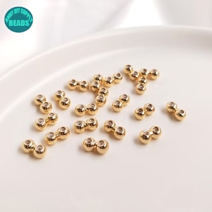 Puede incluir: Primer plano de un grupo de cuentas doradas de doble cara. Las cuentas están dispuestas en un patrón aleatorio sobre una superficie blanca.