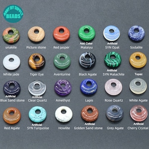 Puede incluir: Surtido de 18 cuentas de piedras preciosas en forma de rosquilla en varios colores, incluyendo jaspe rojo, aventurina, ojo de tigre, &aacute;gata blanca, lapisl&aacute;zuli, cuarzo rosa, howlite y sodalita. Las cuentas est&aacute;n dispuestas en una cuadr&iacute;cula sobre un fondo gris. El texto "ANNI DIY SUPPLY BEADS" est&aacute; en la parte superior de la imagen.
