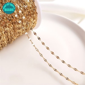 May include: Gold chain with oval links, shown on a white surface. The chain is wound around a spool.