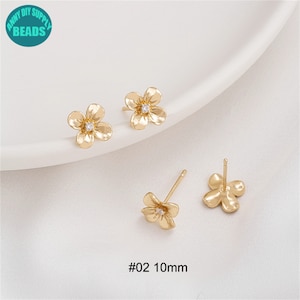 K&ouml;nnte beinhalten: Ein Paar goldene Ohrringe in Blumenform mit einem kleinen, klaren Strassstein in der Mitte jeder Blume. Die Ohrringe sind 10 mm gro&szlig; und mit #02 gekennzeichnet.