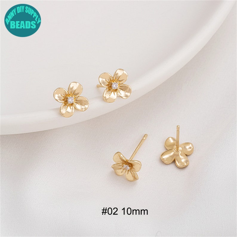 K&ouml;nnte beinhalten: Ein Paar goldene Ohrringe in Blumenform mit einem kleinen, klaren Strassstein in der Mitte jeder Blume. Die Ohrringe sind 10 mm gro&szlig; und mit #02 gekennzeichnet.