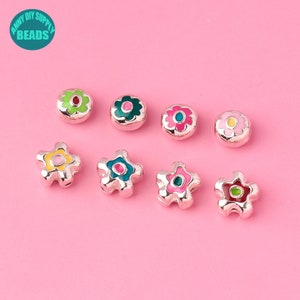 May include: Assortment of colorful enamel flower and star shaped beads. The beads are silver with a variety of colored enamel designs. The beads are perfect for jewelry making or crafting.
