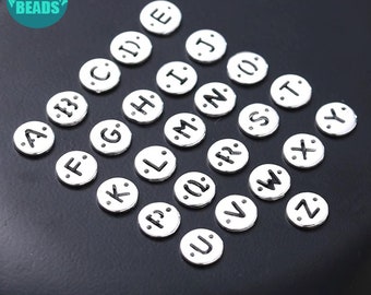 May include: Silver alphabet letter charms, each letter is a separate charm. The letters are in a circle shape with a white background and black lettering. The letters are A through Z.