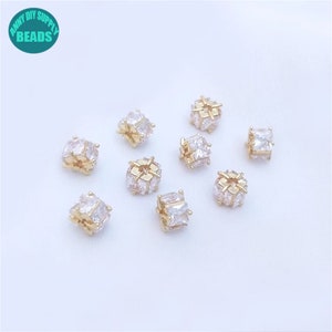 May include: Ten gold-toned spacers with clear cubic zirconia stones. The spacers are square shaped and have a hole in the center.