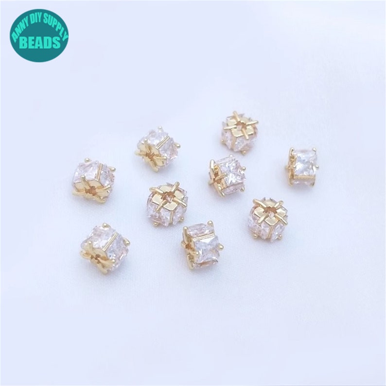 May include: Ten gold-toned spacers with clear cubic zirconia stones. The spacers are square shaped and have a hole in the center.