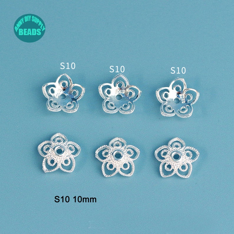 May include: Six silver-colored flower-shaped bead caps, each with five petals and a central hole. The bead caps are labeled "S10" and are approximately 10mm in diameter. The background is a solid light blue.