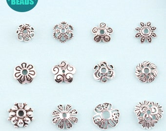 May include: Twelve silver-toned metal bead caps with various ornate designs. The bead caps are arranged in three rows of four.