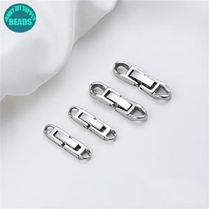 May include: Four silver metal clasps of different sizes are arranged diagonally on a white surface. Each clasp has a rectangular central section and rounded ends with a small loop. The clasps appear to be new and unused.