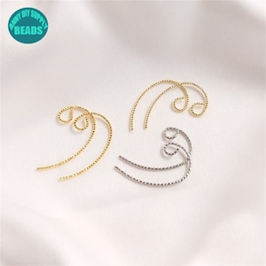 May include: Two pairs of gold and silver ear cuffs. The ear cuffs are made of twisted wire and have a curved shape.