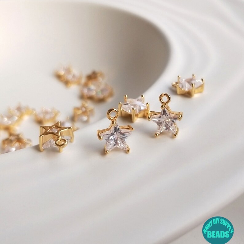 Puede incluir: Encantos en forma de estrella de tono dorado con acentos de cristal transparente. Los encantos tienen un bucle para sujetar a joyas u otras manualidades.