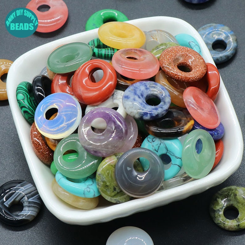 Puede incluir: Un bol lleno de cuentas de piedra preciosa en forma de donut de colores. Las cuentas est&aacute;n hechas de varias piedras naturales, incluyendo amatista, turquesa y &aacute;gata. Las cuentas son perfectas para hacer joyas o manualidades.
