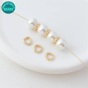 Puede incluir: Anillos de salto retorcidos dorados y cuentas de perlas blancas en una cadena dorada. Los anillos de salto tienen un diámetro de aproximadamente 1,2 cm.
