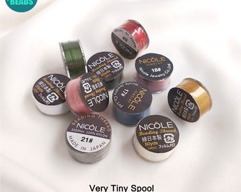 May include: A collection of small spools of colorful beading thread. The spools are labeled "Nicole" and have Japanese text on them. The spools are very small, about the size of a coin.
