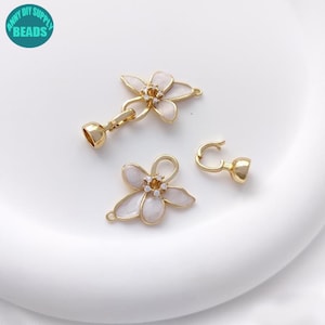 Op de afbeelding: Goudkleurige bloemvormige sieradenonderdelen met witte emaille bloemblaadjes en een centraal kristalaccent. Inclusief een sluiting en een haak. De tekst "ANNY DIY SUPPLY BEADS" is ook zichtbaar.