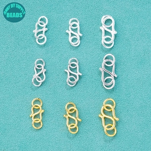 Könnte beinhalten: Eine Auswahl an silbernen und goldenen S-förmigen Verschlüssen für die Schmuckherstellung, angeordnet auf einem türkisfarbenen Hintergrund. Im oberen linken Eck steht "ANNY DIY SUPPLY BEADS" in einem Kreis.