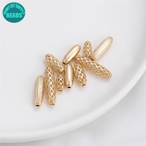 Puede incluir: Un grupo de cuentas de metal de color dorado, algunas con un acabado liso y otras con un diseño texturizado y calado. Las cuentas son de forma ovalada y están dispersas sobre una superficie blanca.