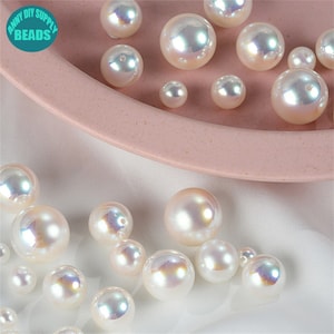 May include: A collection of iridescent white pearl beads in various sizes, displayed on a pink plate. The beads have a pearlescent finish and are perfect for crafting jewelry or other decorative projects.