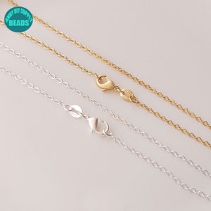 May include: Two silver and gold chain necklaces with lobster clasps. The chains are lying on a white surface.