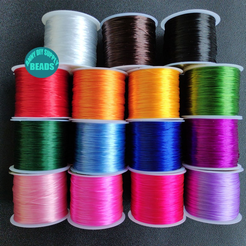 May include: Assortment of 12 spools of elastic string in various colours, including white, brown, black, red, orange, yellow, green, blue, purple, pink, and lavender. The spools are arranged in three rows of four. The text "ANNY DIY SUPPLY BEADS" is printed on a white label.