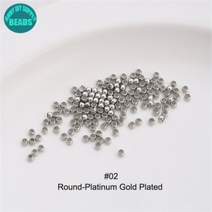 May include: A close-up image of a pile of small, round, silver-coloured beads. The beads are scattered on a white surface. The text "#02 Round-Platinum Gold Plated" is printed below the beads.