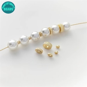 May include: A strand of white pearl beads with gold spacers. The spacers are different sizes and have a ridged design. The beads are strung on a thin gold cord.