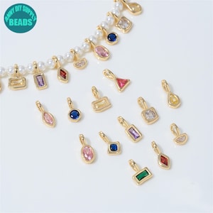 May include: A collection of gold-toned metal charms featuring various geometric shapes and colourful inset crystals, including rectangular, oval, triangular, and teardrop designs. Some charms are attached to a white pearl beaded strand.