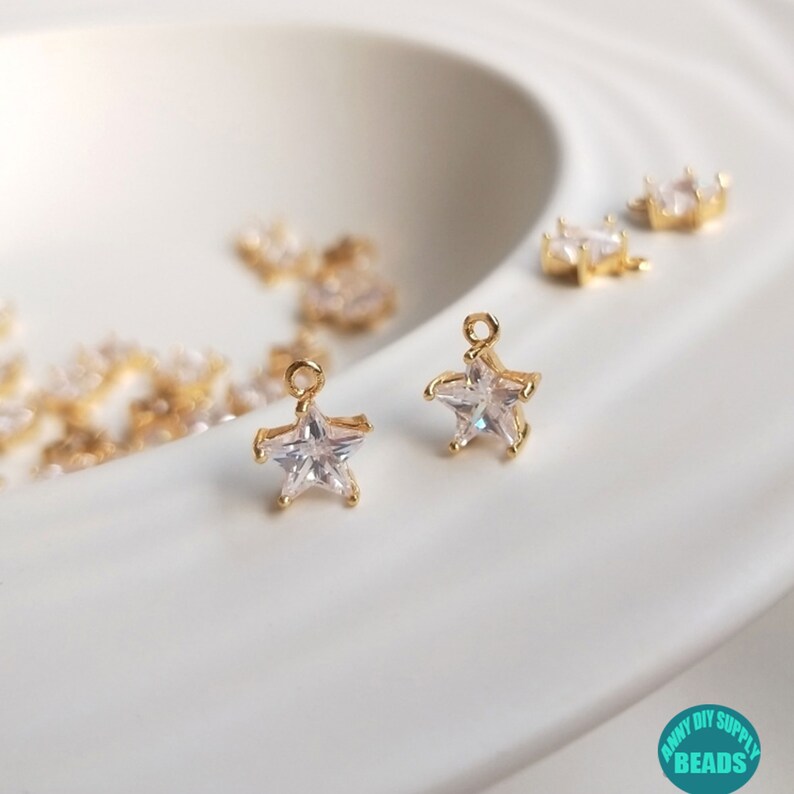 Puede incluir: Dos abalorios en forma de estrella de tono dorado con acentos de cristal transparente. Los abalorios tienen un bucle en la parte superior para sujetarlos a joyas u otras manualidades.