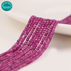 Op de afbeelding: Een streng roze robijn edelsteen kralen, elke kraal is gefacetteerd en vierkant gevormd. De kralen zijn geregen op een doorzichtige draad en zijn klaar voor het maken van sieraden.